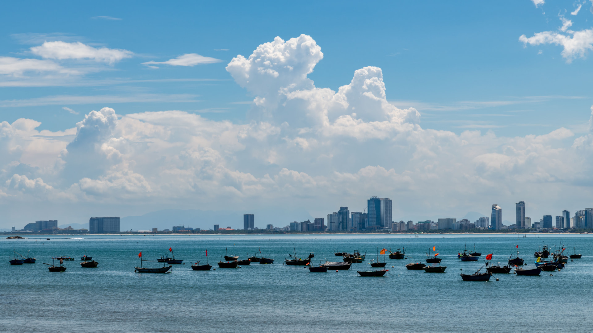 Fishing boats moored in the blue bay off Da Nang, Vietnam, with the city skyline behind